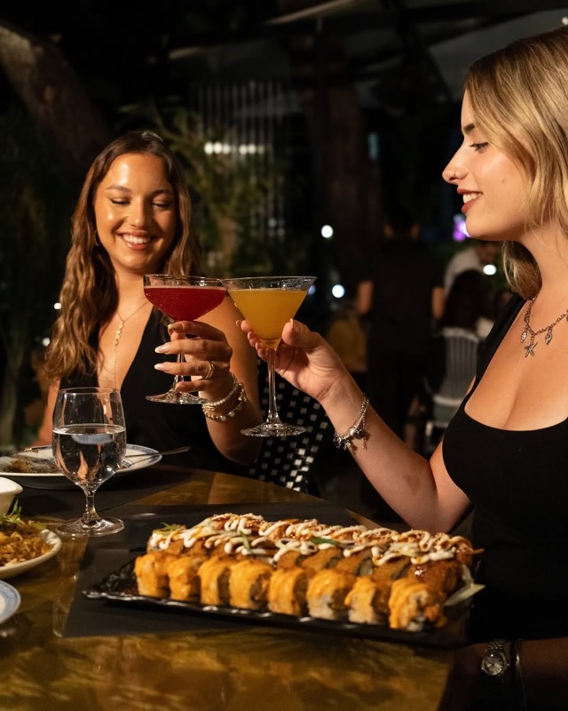 Δύο φίλες τσουγκρίζουν cocktails πάνω από πιατέλα sushi στο Nama
