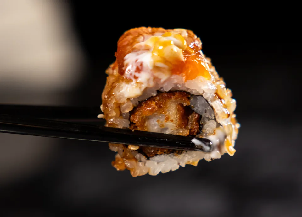 Κοντινή λήψη ενός sushi roll με σάλτσα, κρατημένου με chopsticks