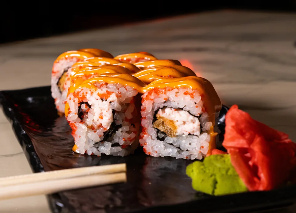 Sushi rolls με πορτοκαλί σάλτσα σε μαύρη πιατέλα, με wasabi και ginger